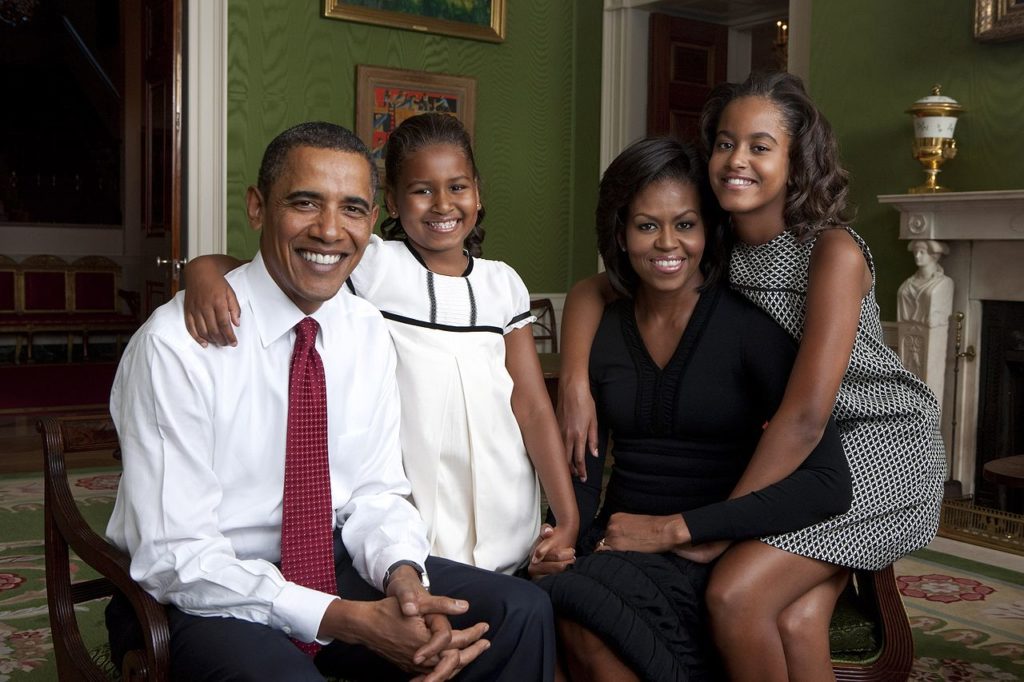 US President Barack Obama with his daughters and wife, Michelle. They are seated and smiling broadly.